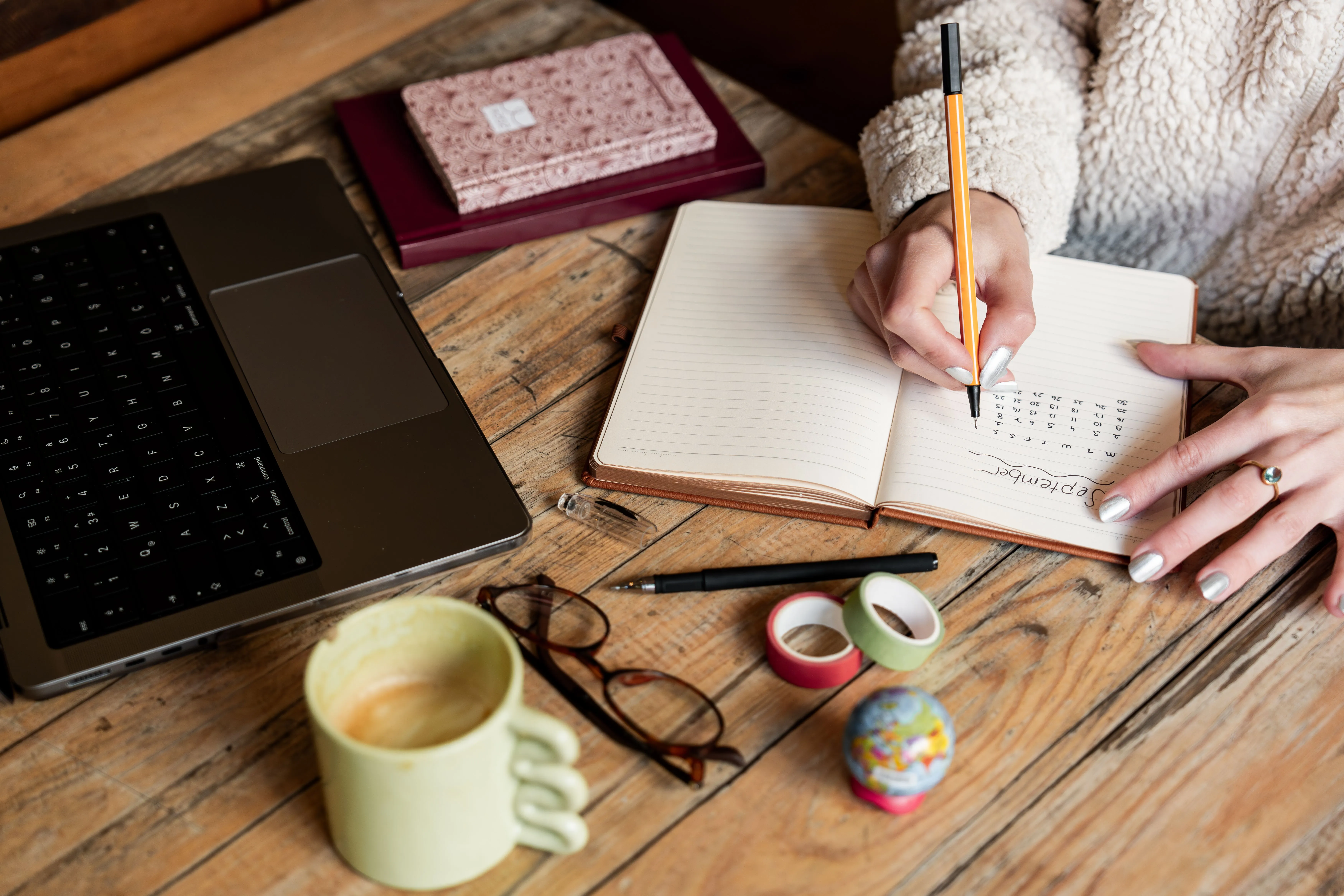 A person planning the next newsletter issue in a notebook beside a laptop and coffee