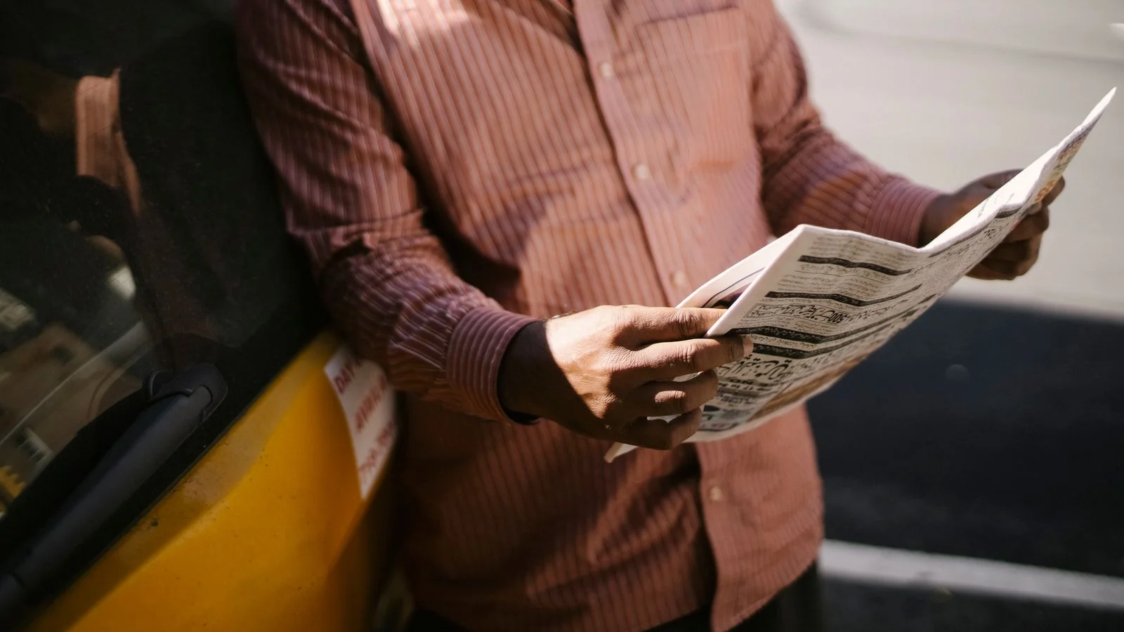 Man reading a folded newspaper on a sunlit street, the reader an announcement has five seconds to catch