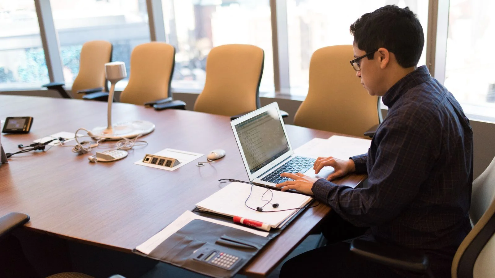 Professional working at a laptop in a bright conference room, drafting an announcement for review