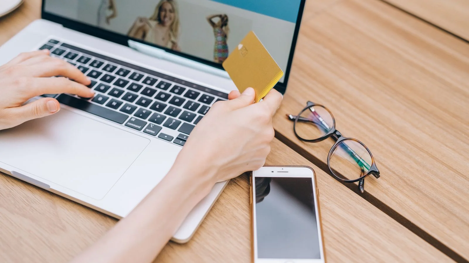A person making an online purchase with a credit card beside a laptop.