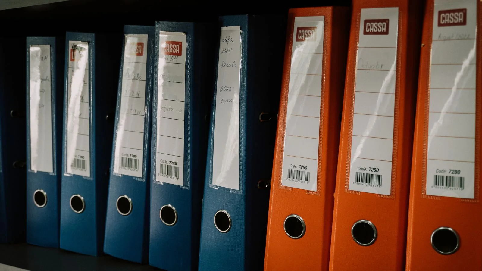 Rows of labeled binders on an office shelf, the paperwork behind a thin online footprint.