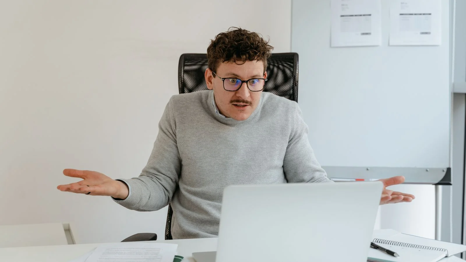 A man gesturing at his laptop during a video call, the desk-bound client most therapist sites never name