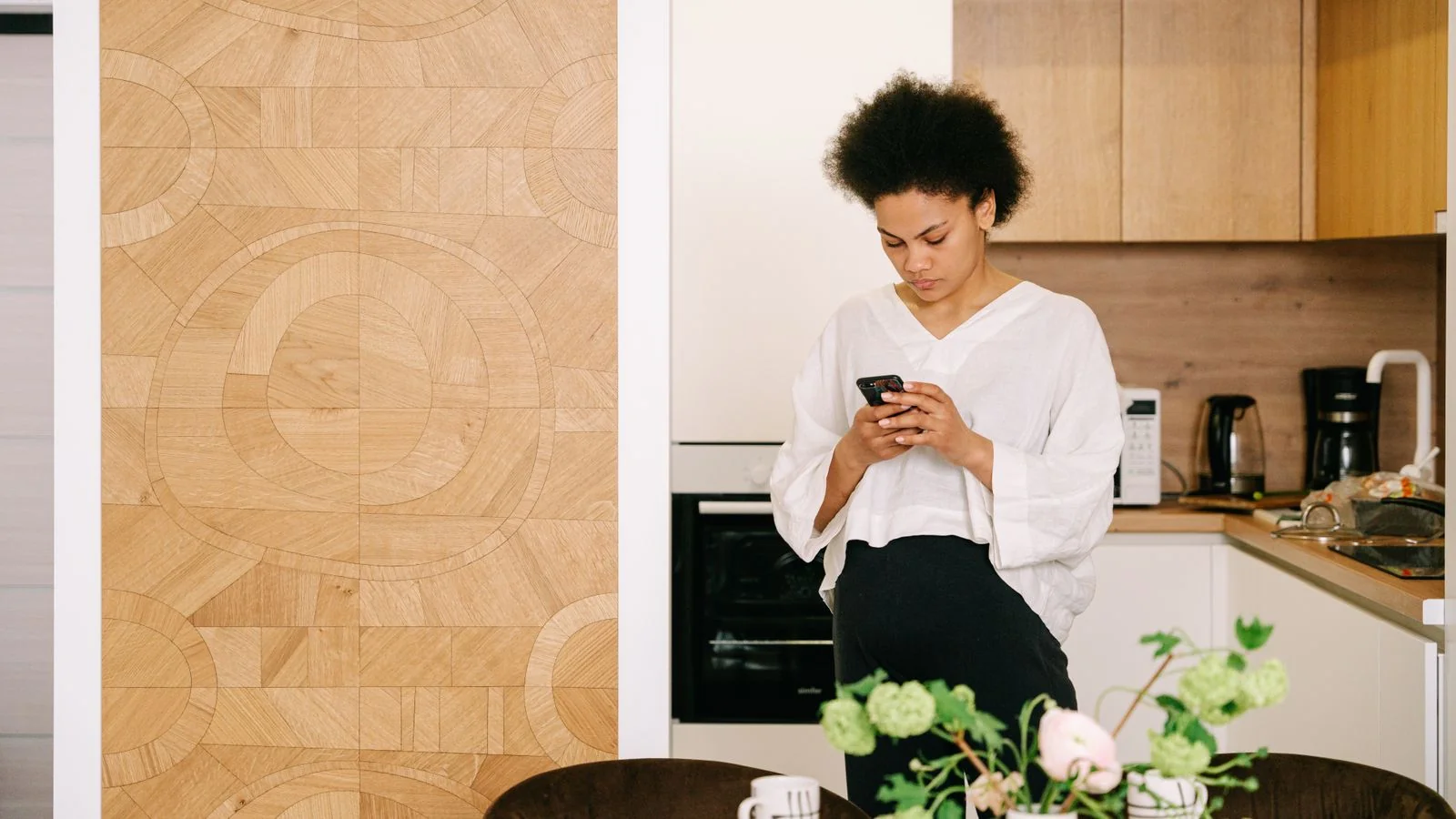 A person standing in a kitchen looking at their phone while preparing food.