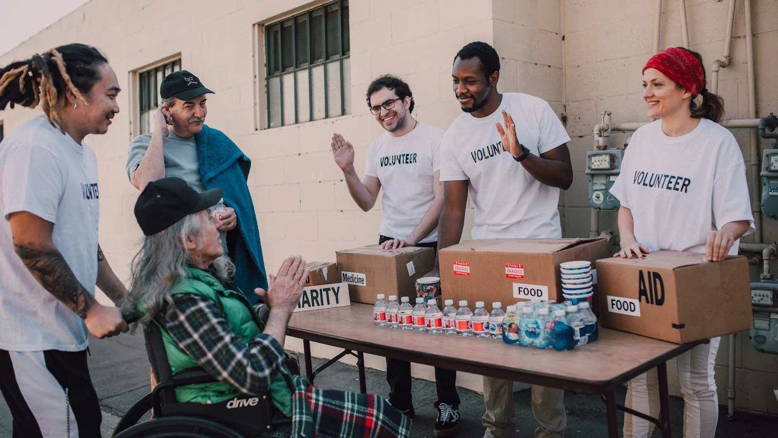 Volunteers handing food and supplies to a person in a wheelchair outdoors