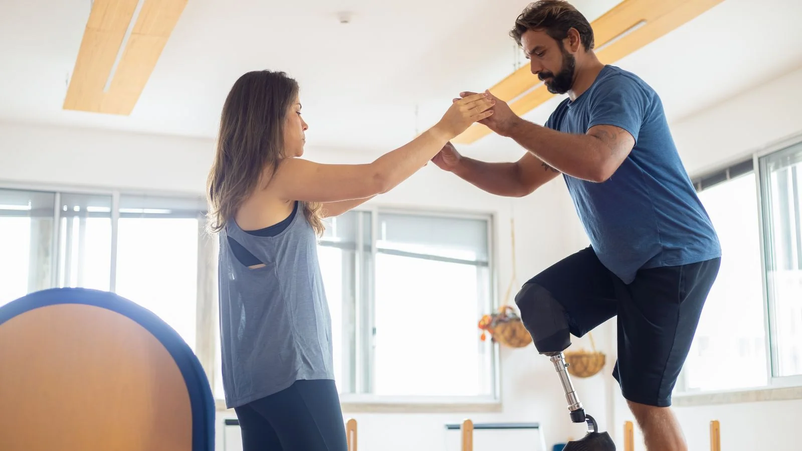 A man working with a therapist in a bright gym, the clinical adjacency Pilates studios describe badly