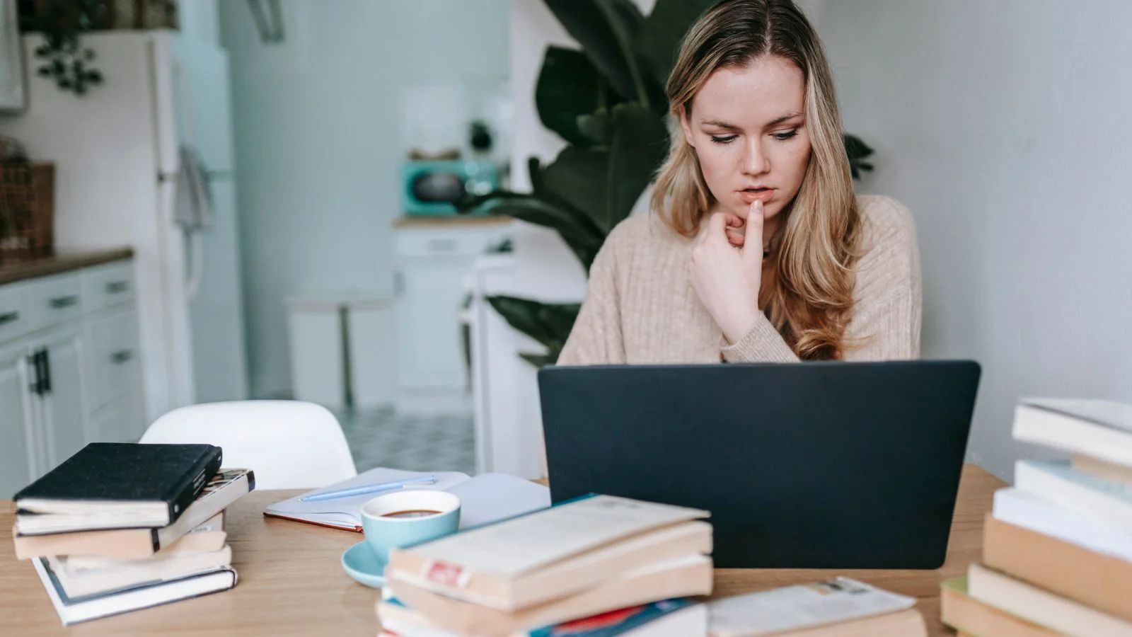 A woman researching on a laptop at a table, the comparison happening before anyone calls your studio