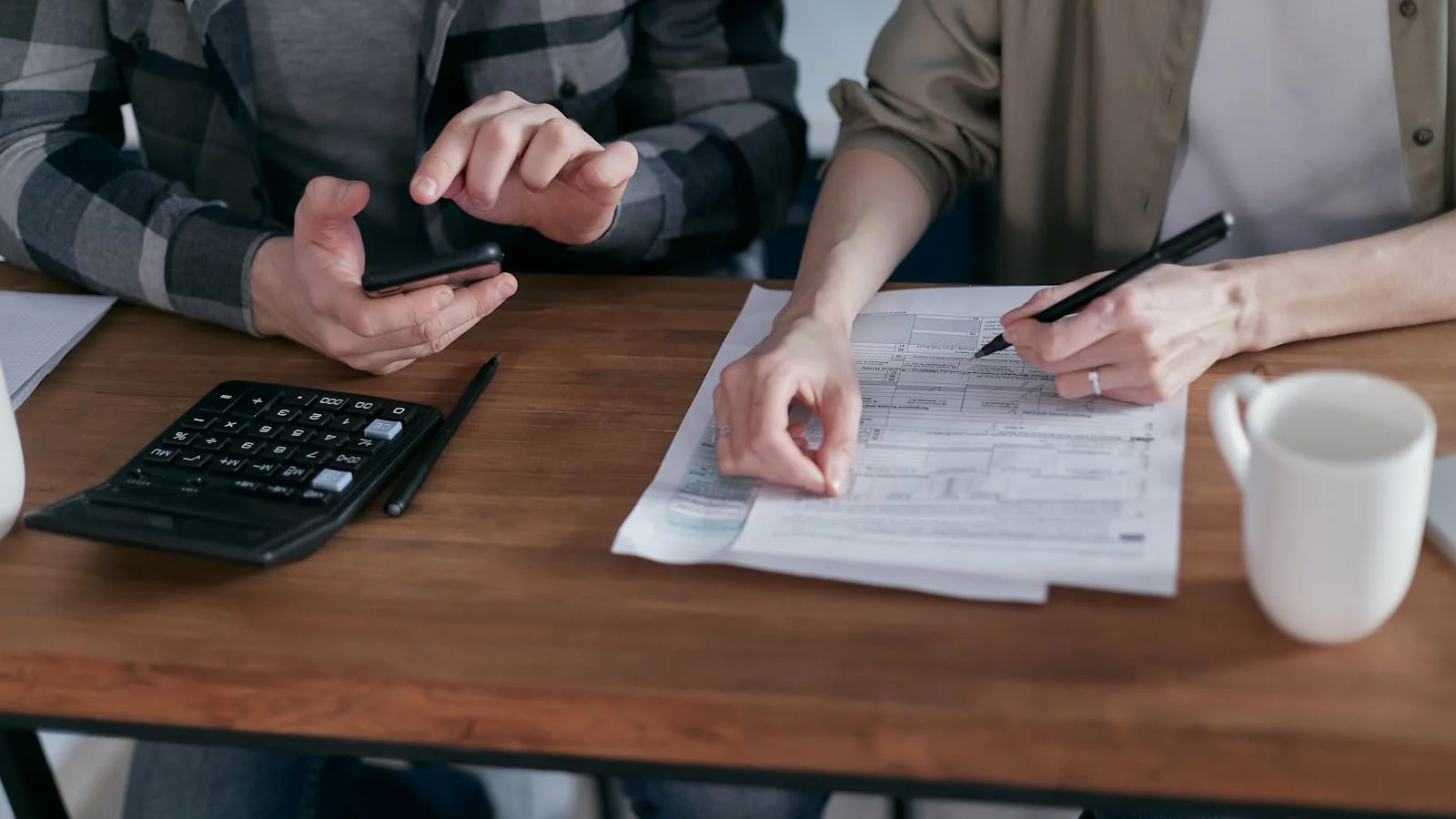Two professional services partners reviewing analytical documents together at a desk, one writing in a notebook beside a calculator.