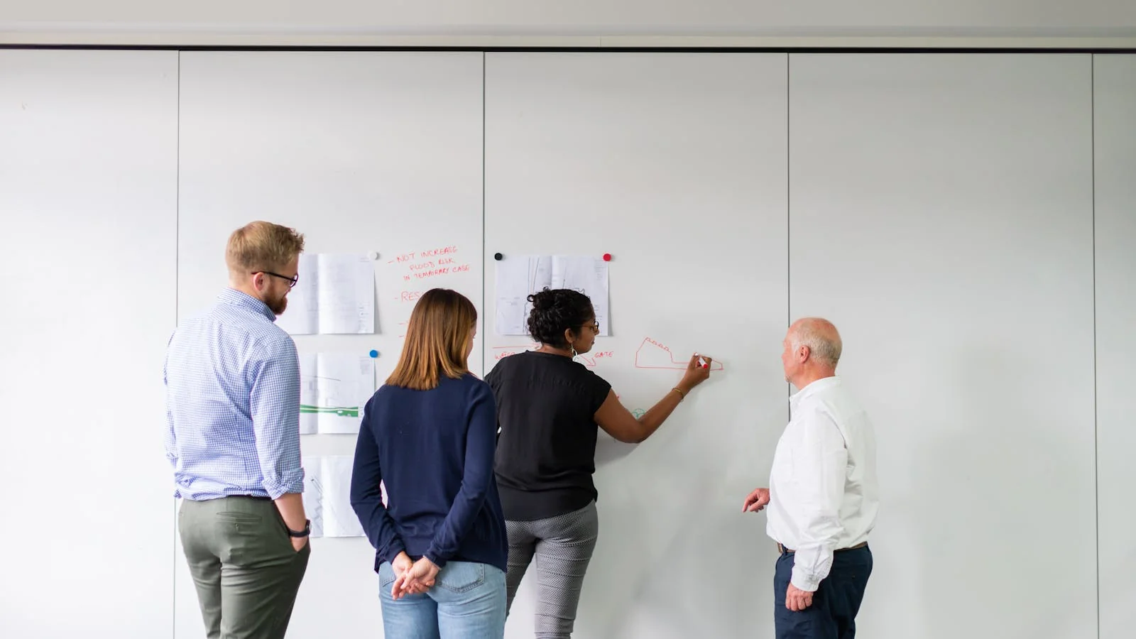 A diverse team of professionals engaged in strategic planning around a whiteboard inside a consulting firm office.