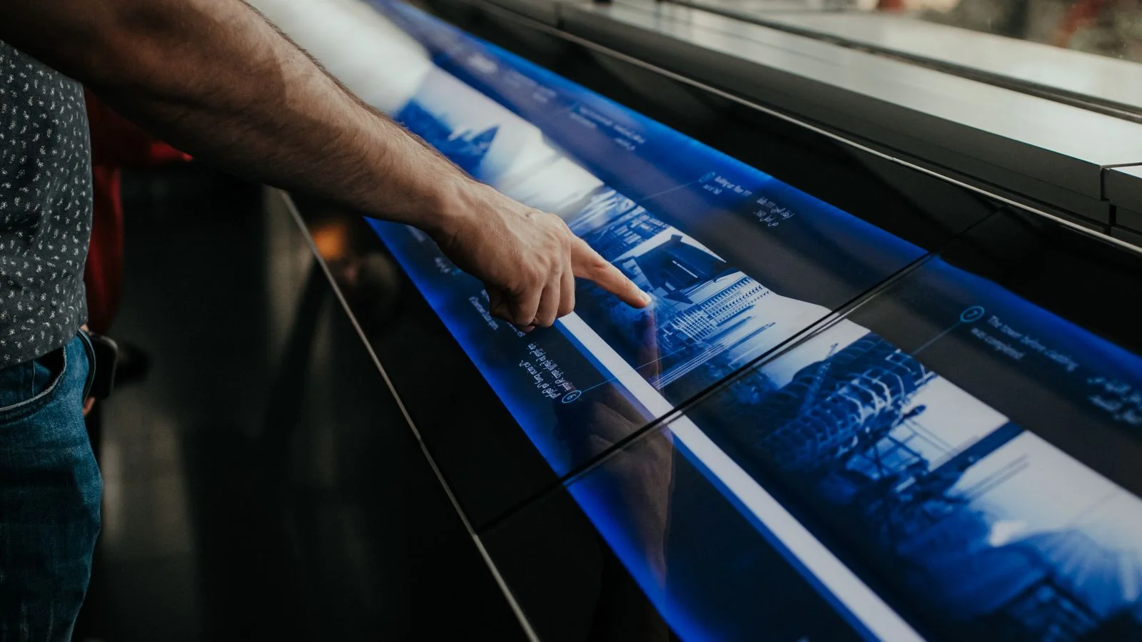 Person tapping a touchscreen kiosk displaying a building interface in a modern lobby