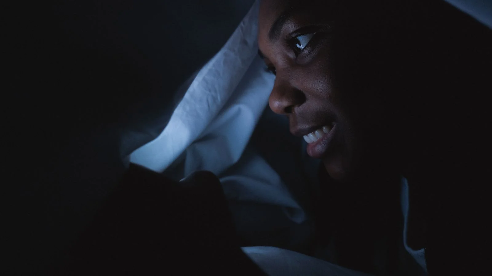 A person sitting in a dark bedroom typing a long message into their phone