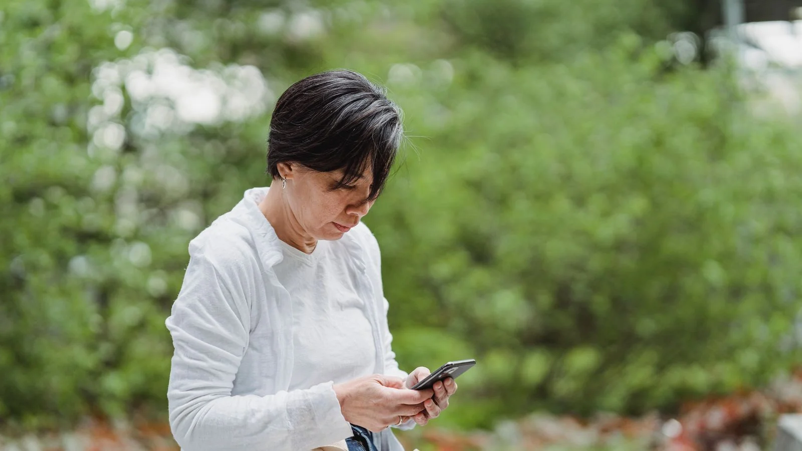 A woman checking her smartphone outdoors while searching for a local sign company.