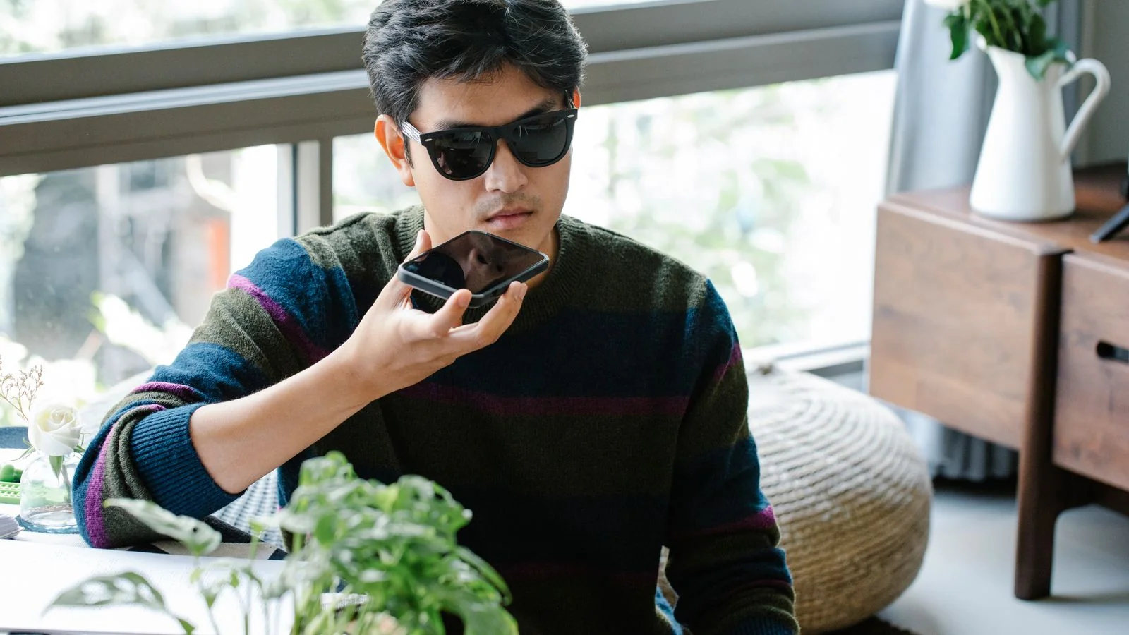 A man using a smartphone's voice assistant to ask a question indoors.