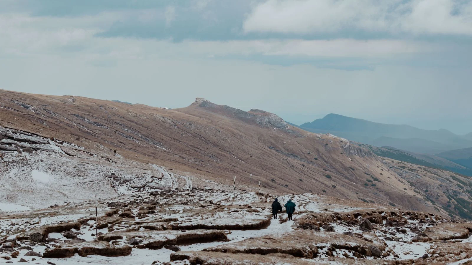 Hikers on a snowy trail in the Bucegi Mountains, the conditions most operators soften and travelers most need to know.