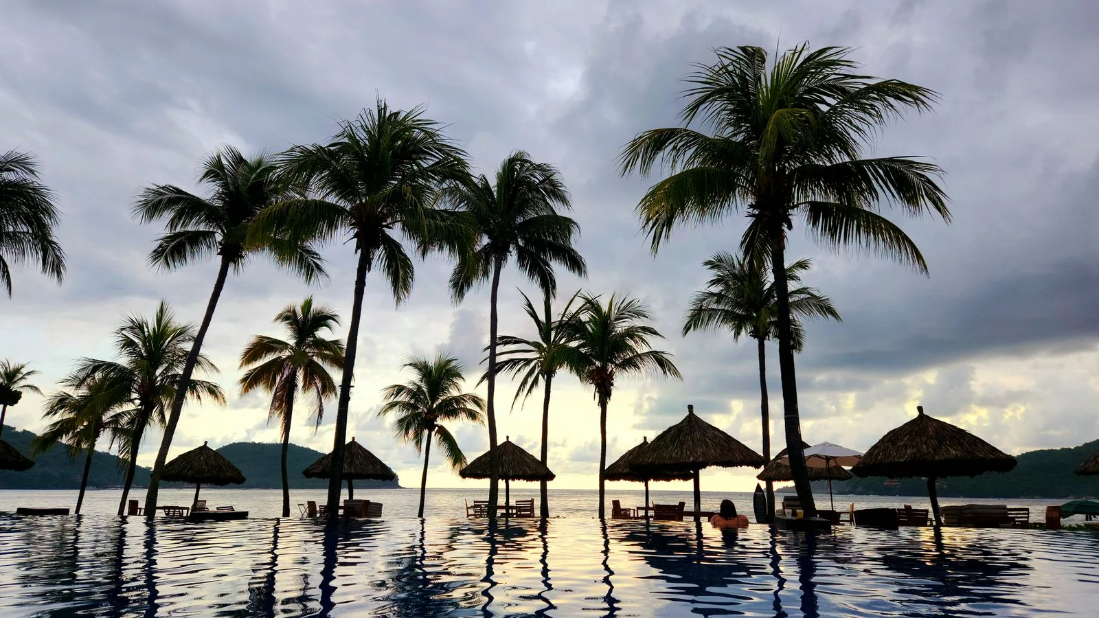 A tropical beach at sunset with palm trees and umbrellas, the specific kind of trip a model can attach to a specific name.