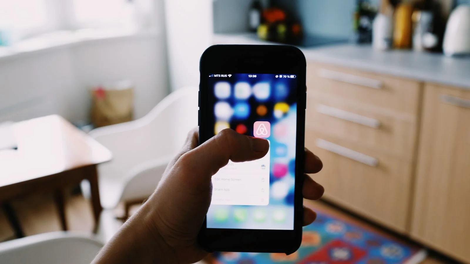 A person tapping a search app on a phone in a bright kitchen.
