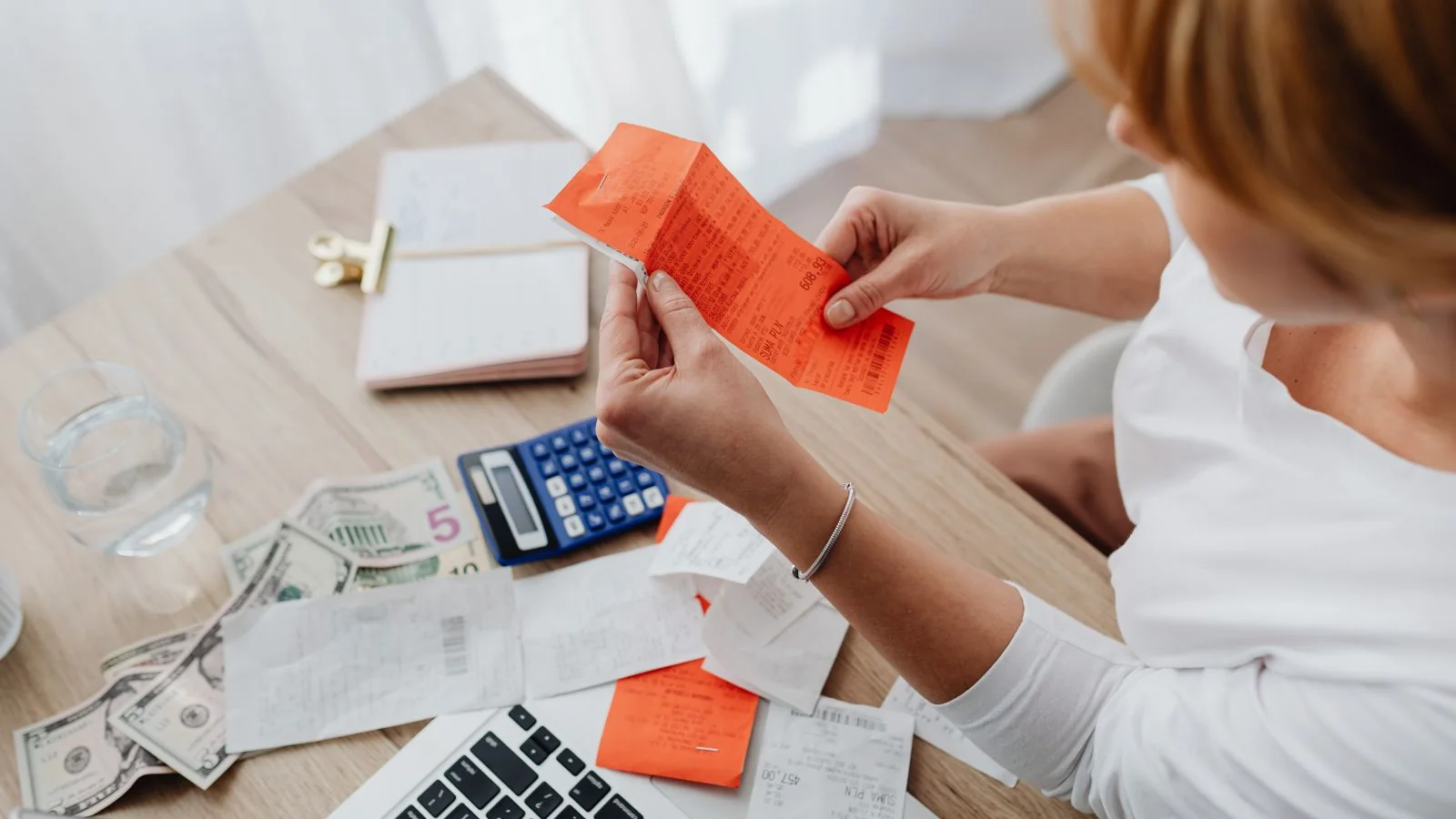 Woman working through receipts with a calculator at a home office desk