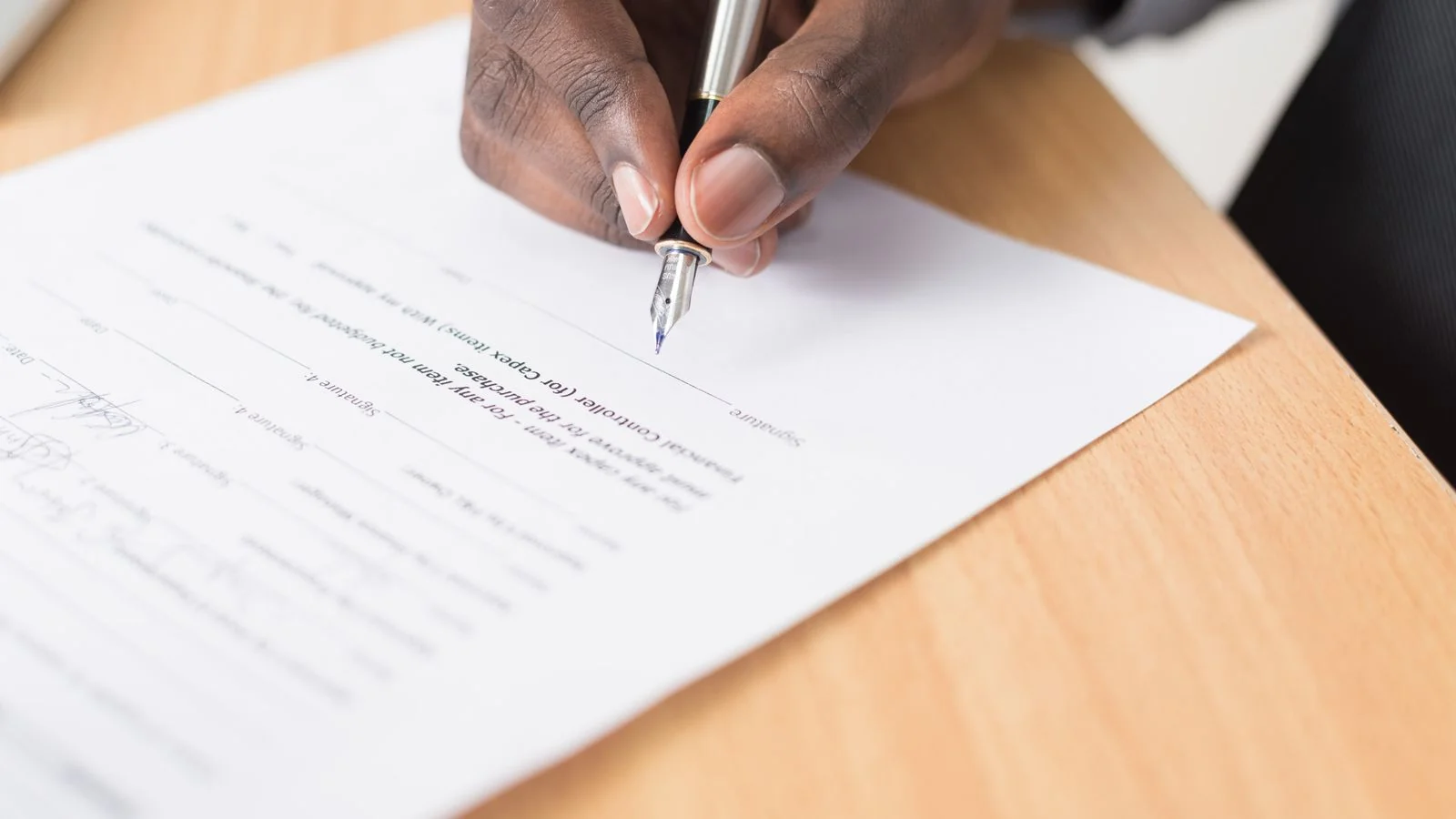 Hand signing a document at a desk, the moment a written apology gets approved
