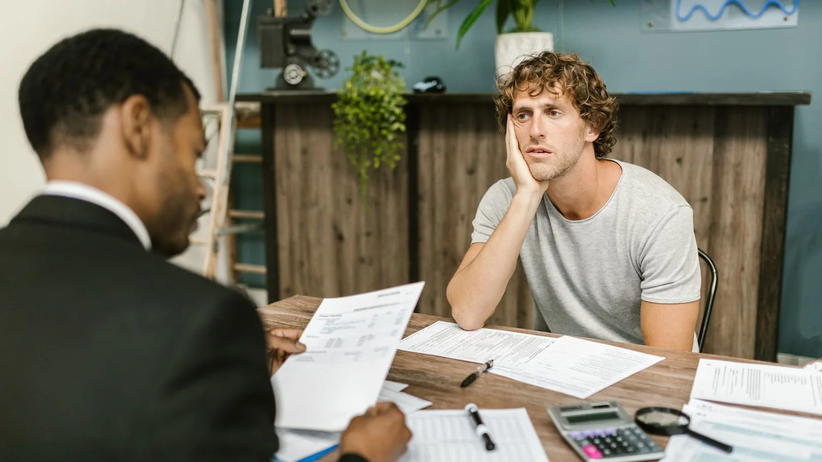Stressed man across a desk from a professional during a tense paperwork discussion