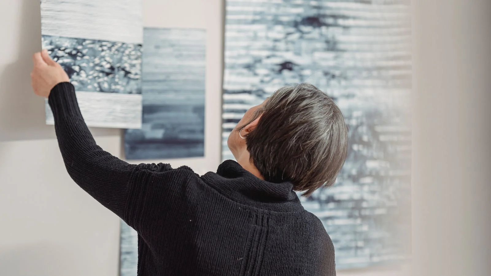 Woman arranges abstract art pieces on a gallery wall while installing an exhibition