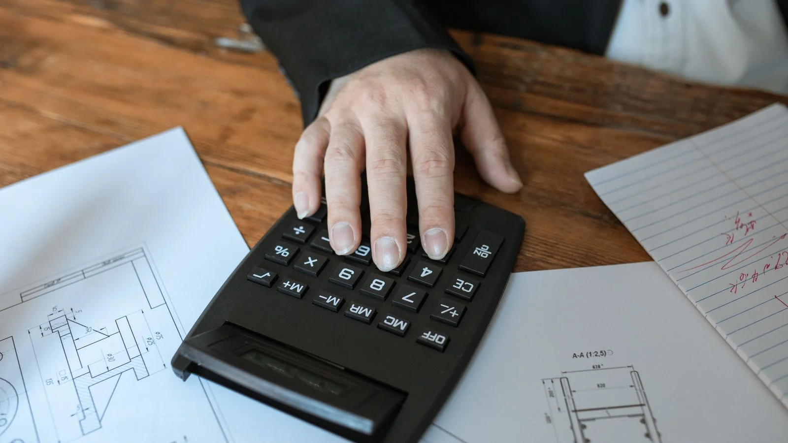 Hand using a calculator on top of architectural blueprints to work out costs
