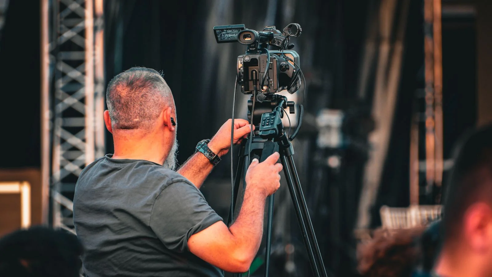 A cameraman filming an outdoor event from behind, the kind of supplemental footage that fills a news package
