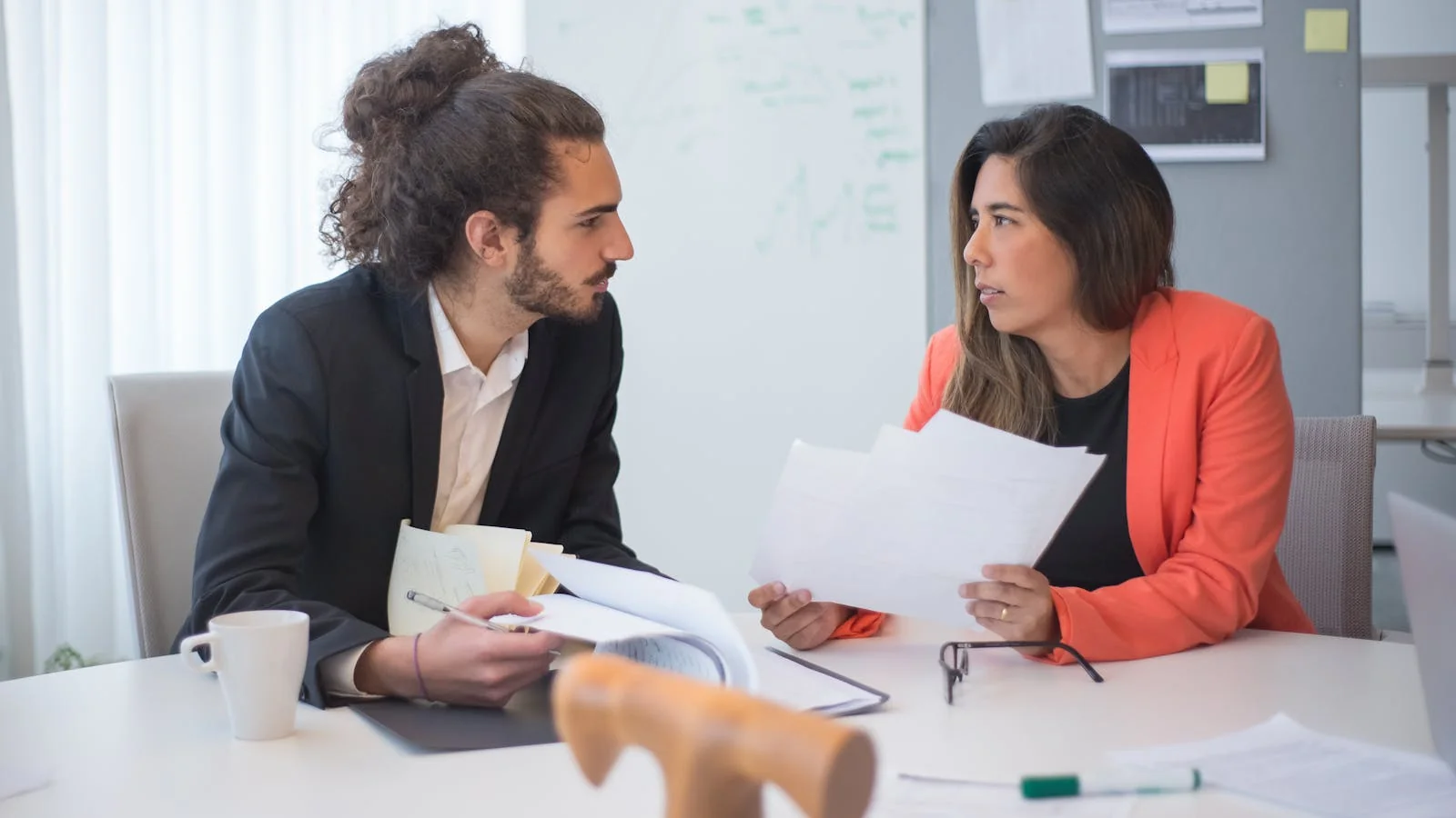 Two colleagues reviewing a customer complaint together at an office table with documents and coffee.