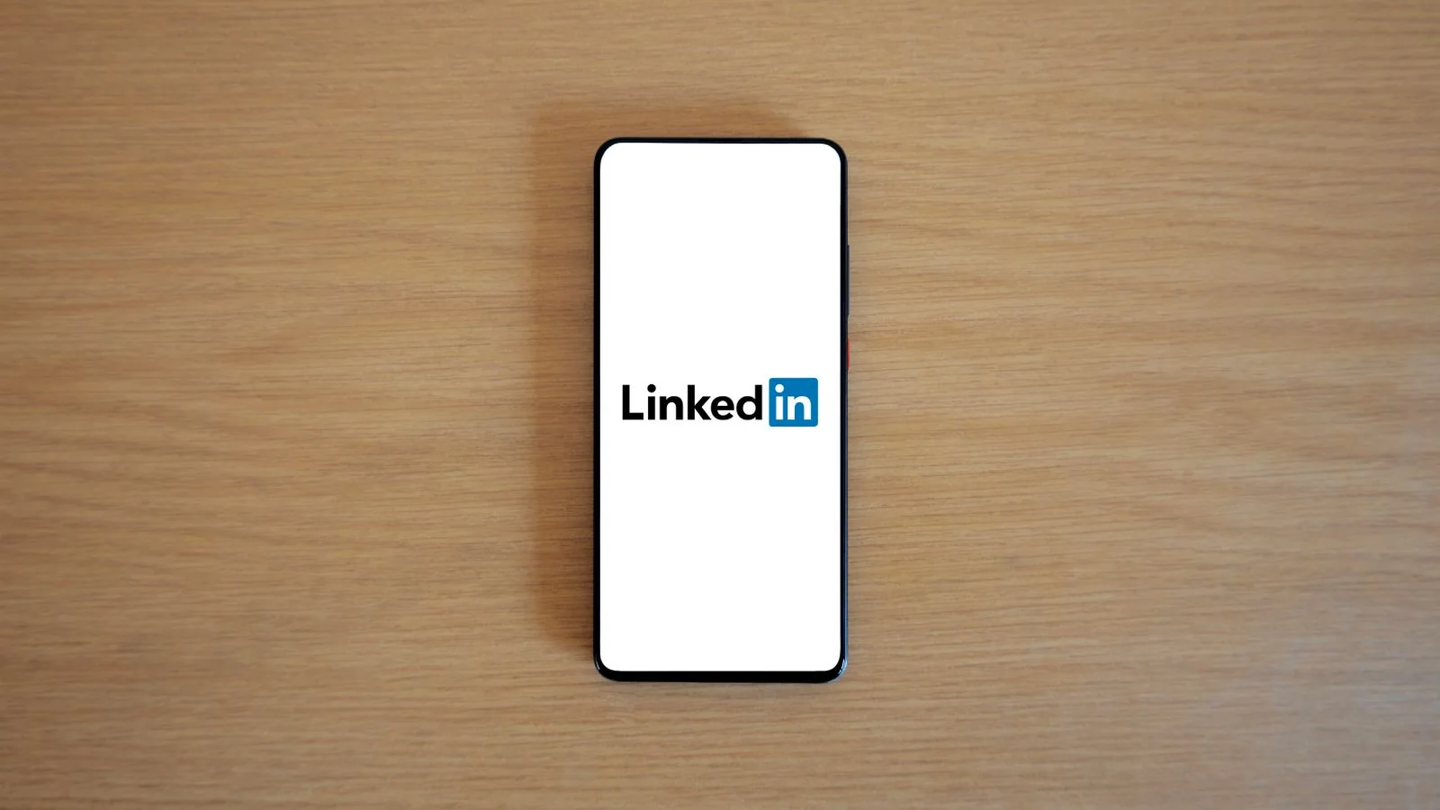A person holding a smartphone showing a LinkedIn profile on a desk