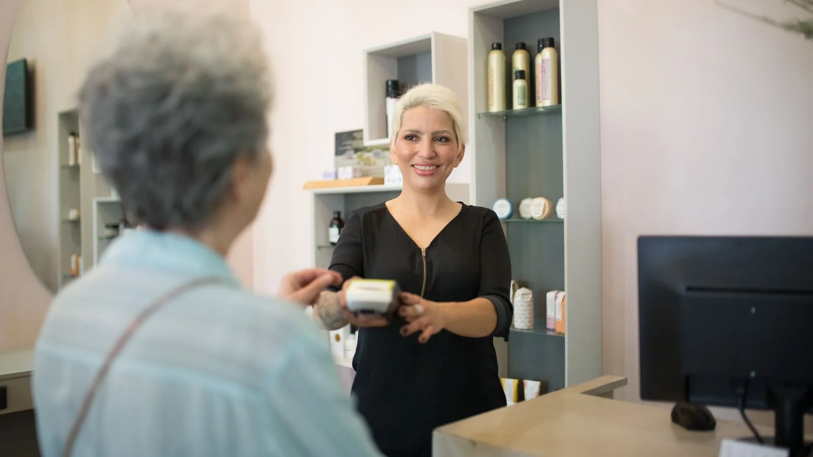 Hairdresser helping a client pay at the front desk of a modern salon