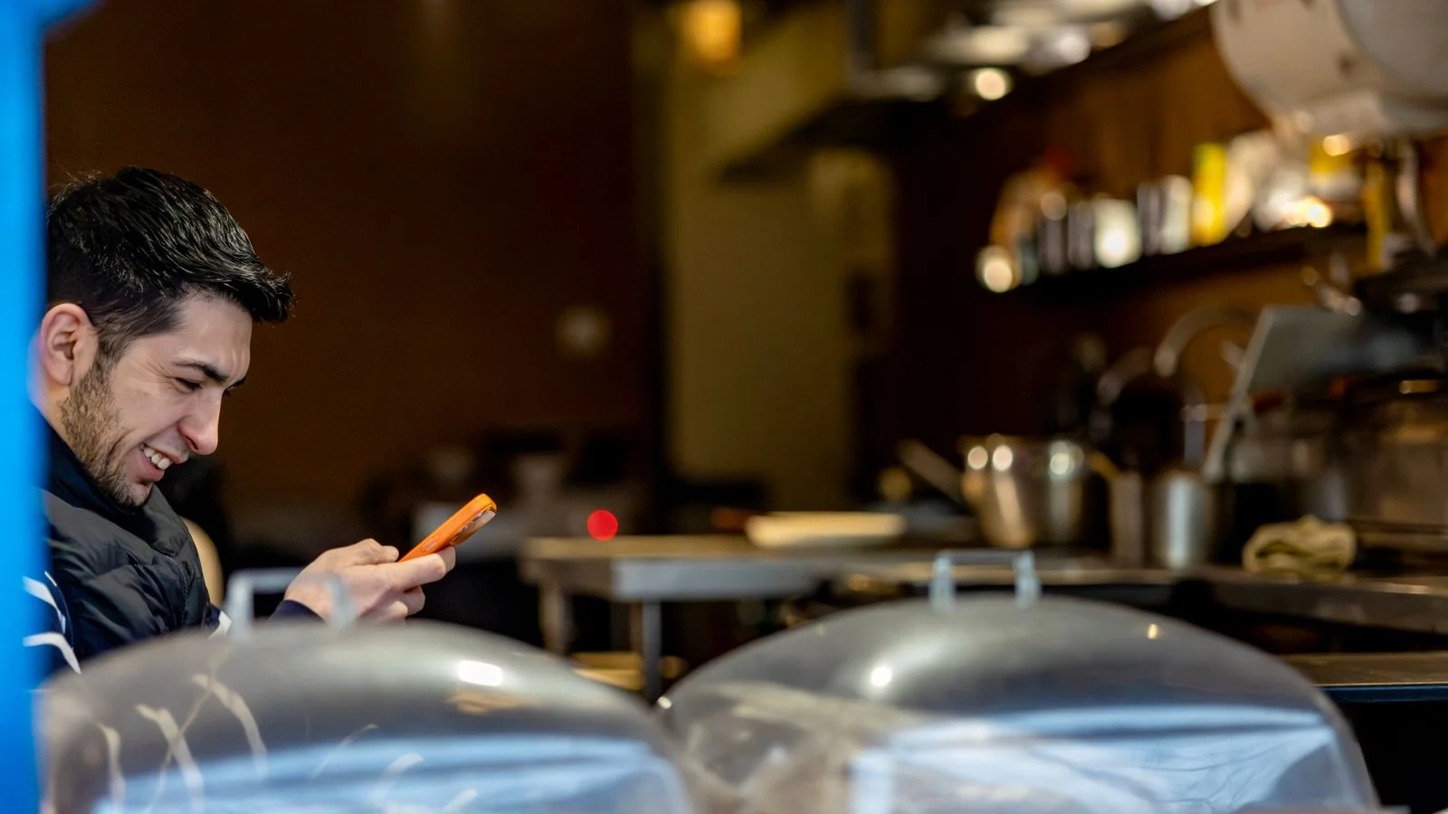 Smiling man in a warm café reads a text on his phone, the moment a review request lands