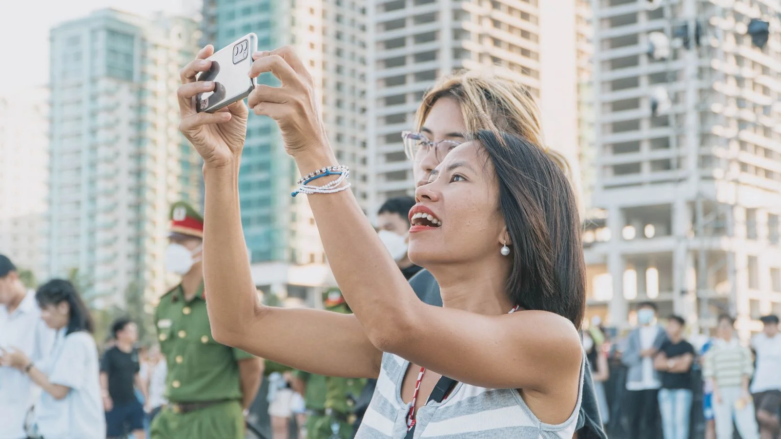 Woman taking a photo on her phone on a busy city street, one of millions of mobile social users
