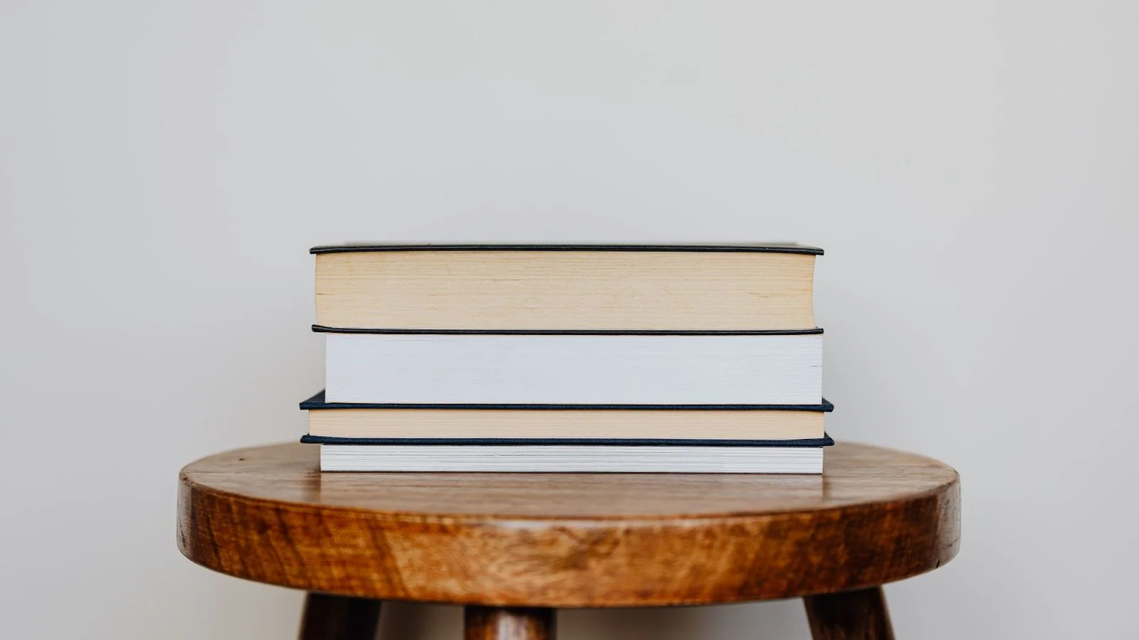 Stack of hardcover books on a round wooden table against a beige wall