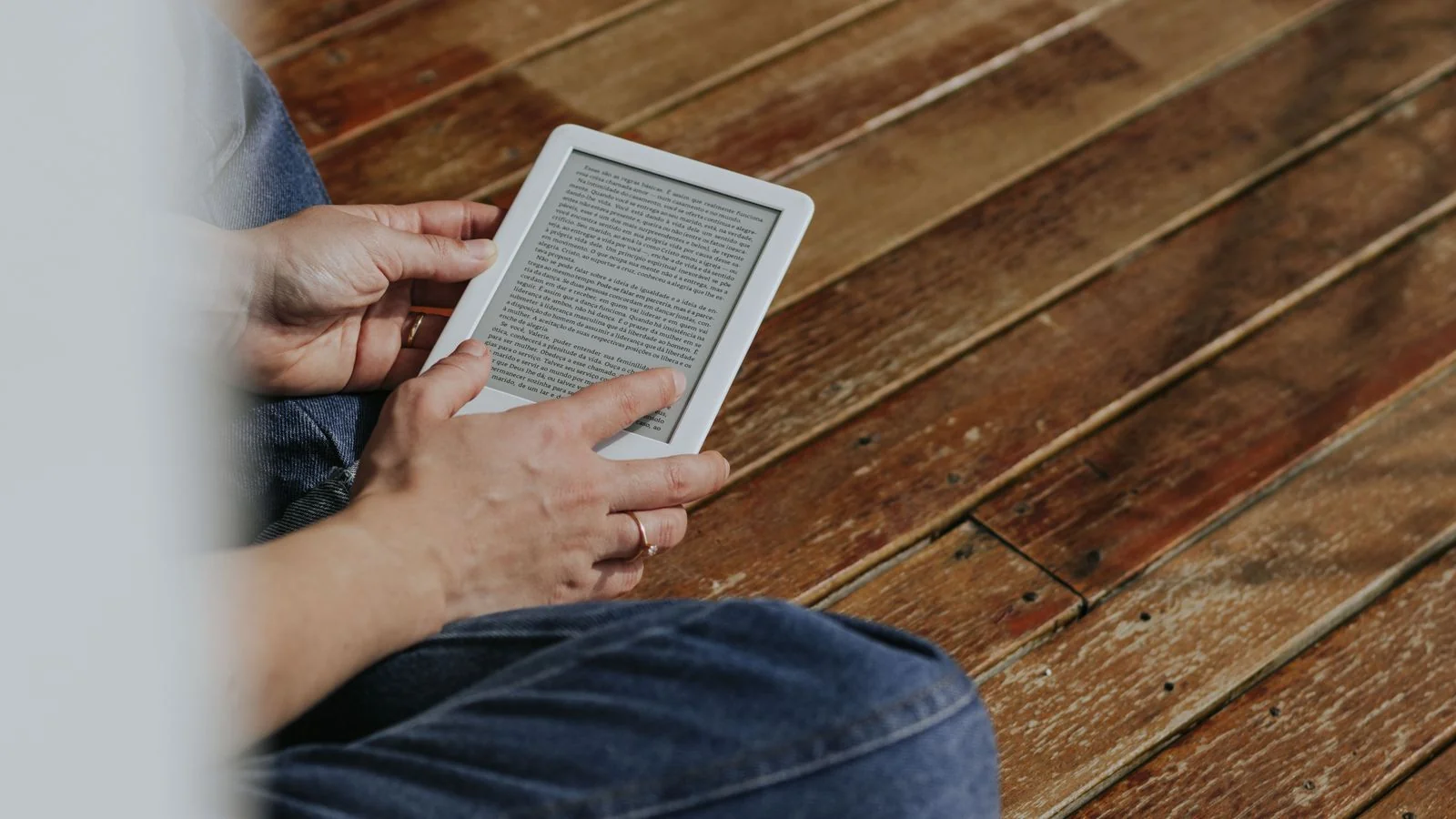 Hands holding an e-reader on a wooden floor during a casual reading moment