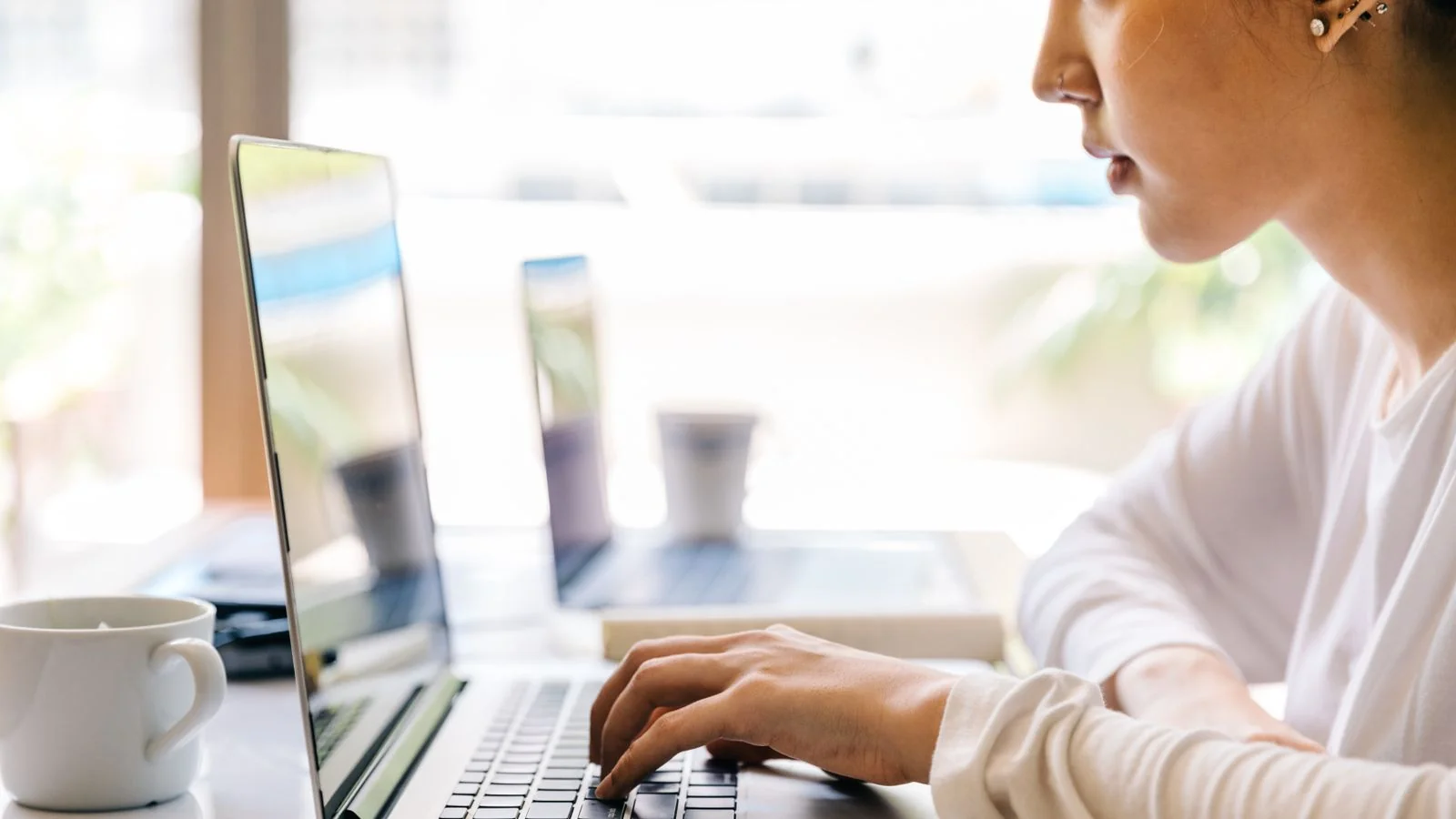 Woman typing on a laptop in a cafe, browsing search results for a company name