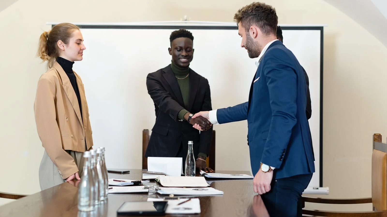 Business professionals shake hands in a meeting room after a certification opens a closed deal