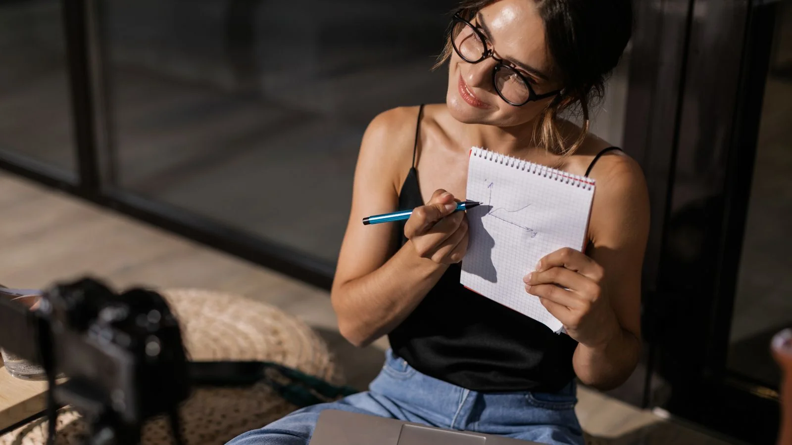 A creator working at a laptop with a camera and notepad, building content engineered to be cited
