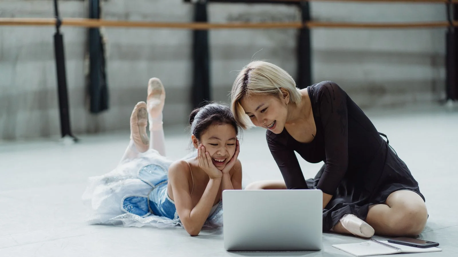 A dance instructor sitting with a young student and a laptop between classes