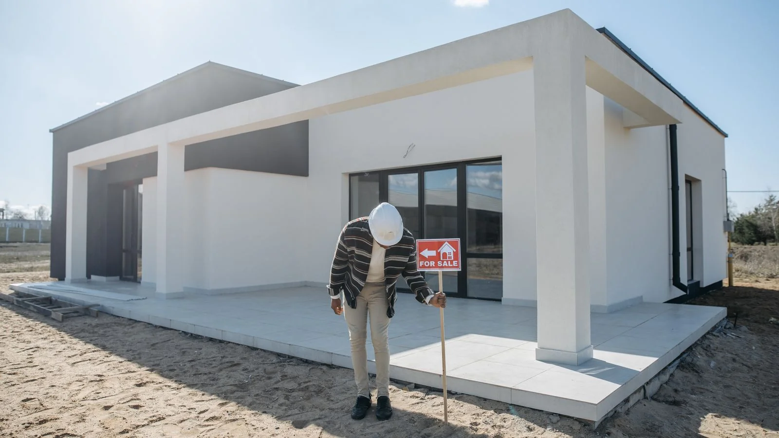 Real estate professional in a hard hat standing beside a newly built home on a finished lot.
