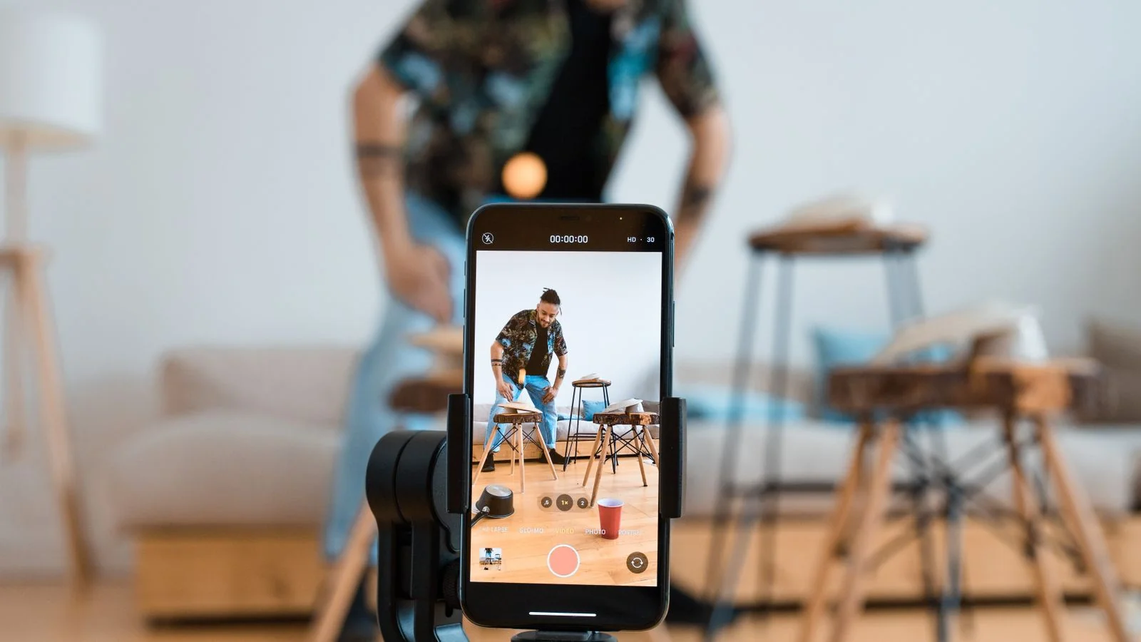 A man recording video on a tripod-mounted smartphone in a living room, the walkthrough format sellers need.