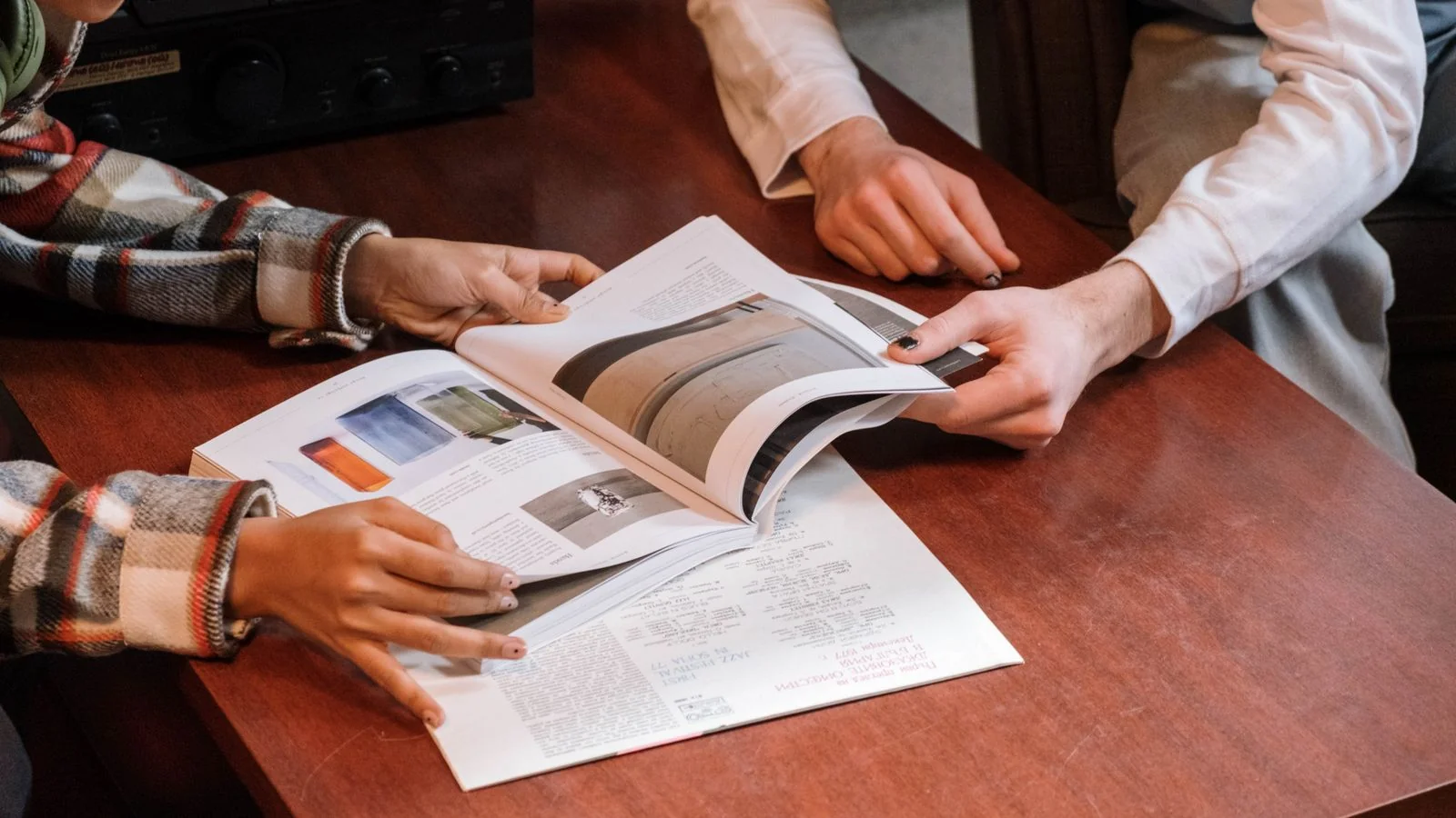 Two people reviewing printed pages together at a wooden table, the feedback loop that separates a method from a lecture