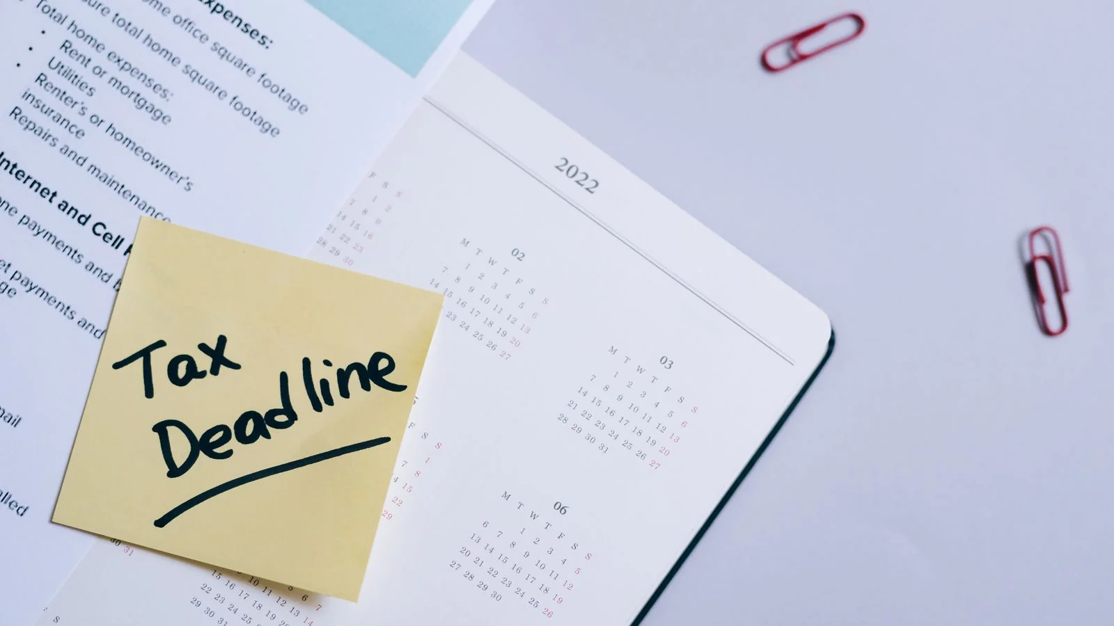 A sticky note marking a tax deadline on a calendar beside financial documents.