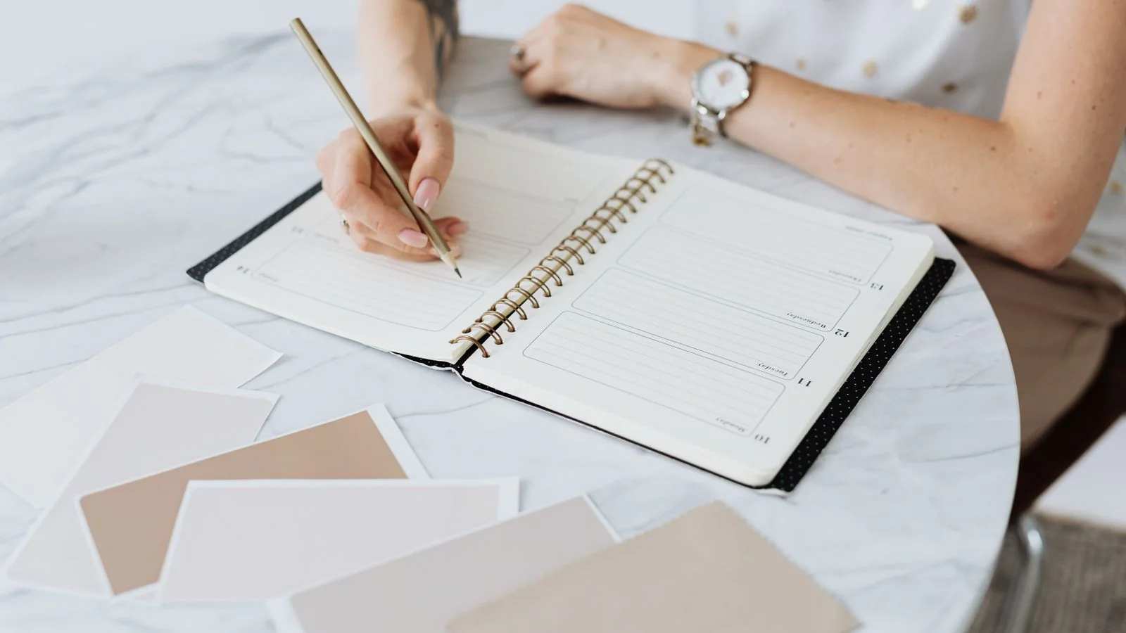 A woman writing in a planner at a marble table, the annual review that keeps a small content library current.