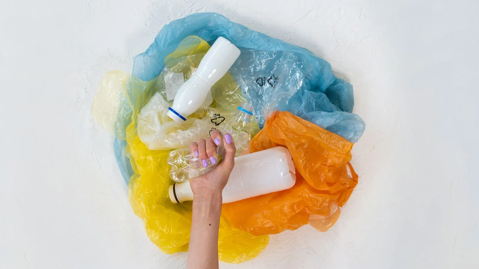 Hand holding a fistful of mixed plastic waste, the material a resident has to sort before it reaches the line.
