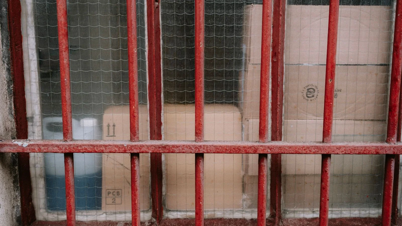 Cardboard boxes stacked behind a red metal grid inside a storage warehouse.