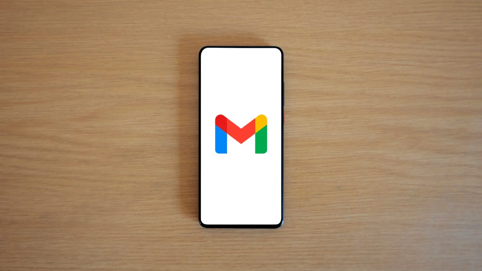 Smartphone showing an email app on a wooden desk, the channel a wire scam arrives through.
