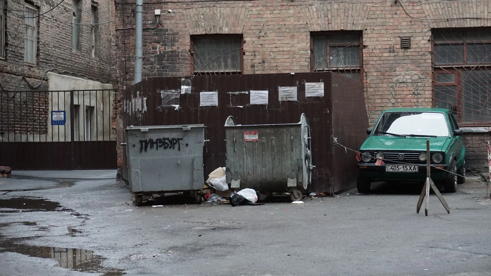 Alley with overflowing garbage bins and scattered debris, the cleanup job that starts with a dumpster search.