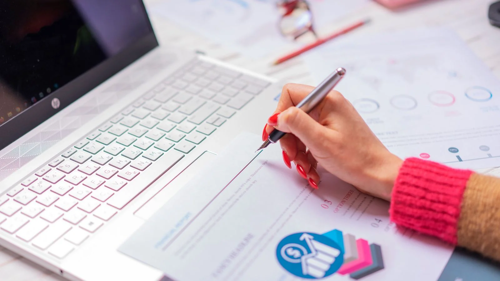 A marketer analyzing budget figures and diagrams on a laptop and printed sheets at a desk