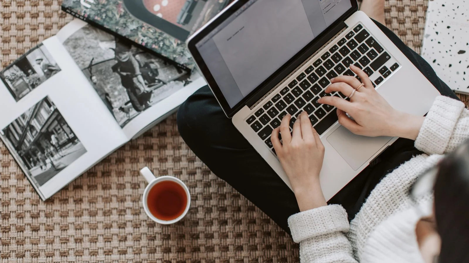 A freelancer in a warm sweater working from the floor with a laptop and a cup of tea