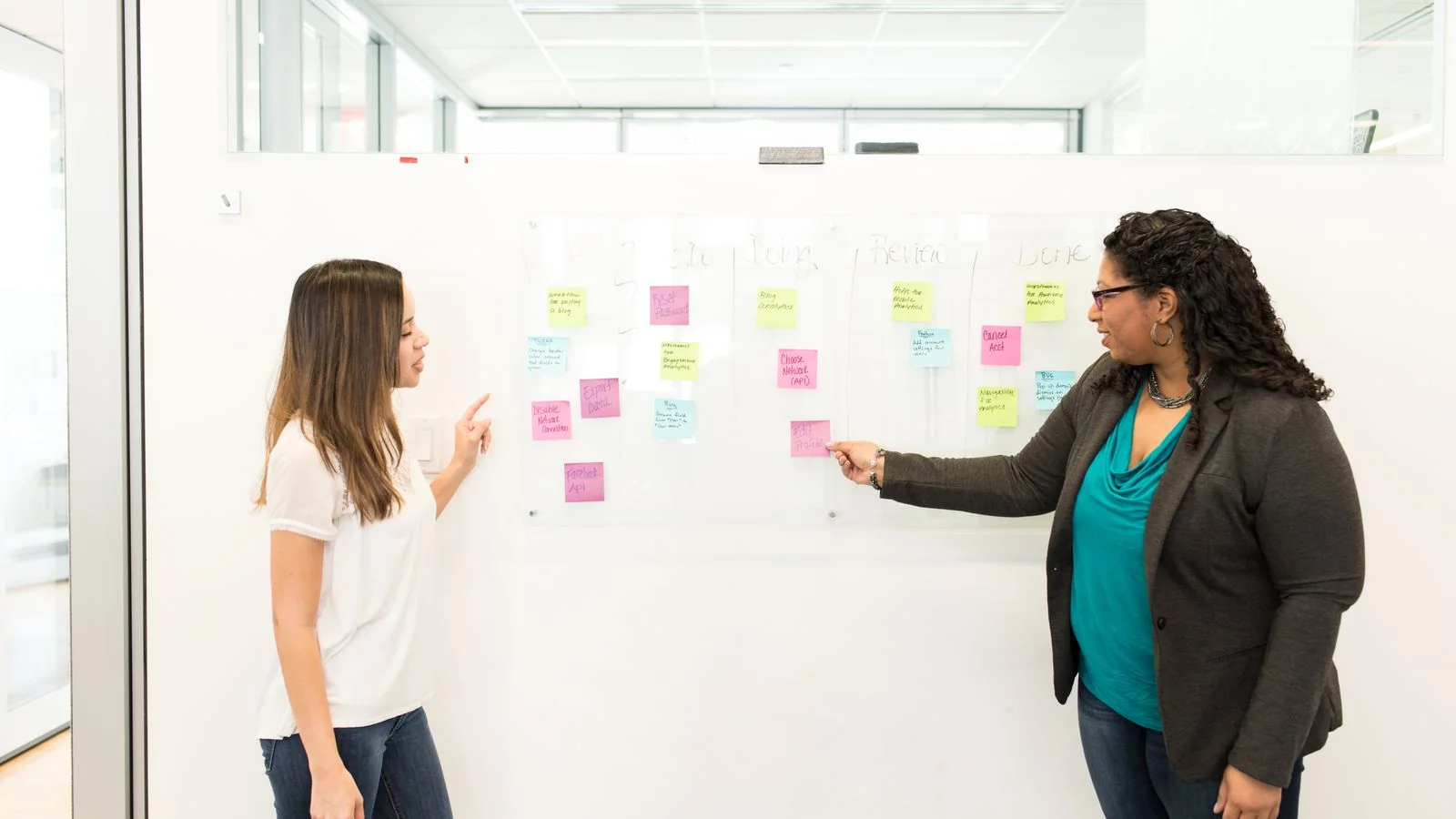 Two colleagues debating sticky-note placements on an office whiteboard mid-planning