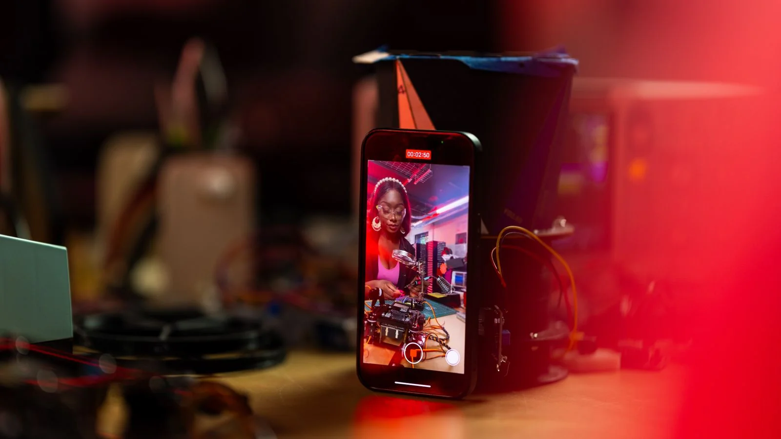 Woman recording a tech tutorial on her smartphone at a desk full of gear