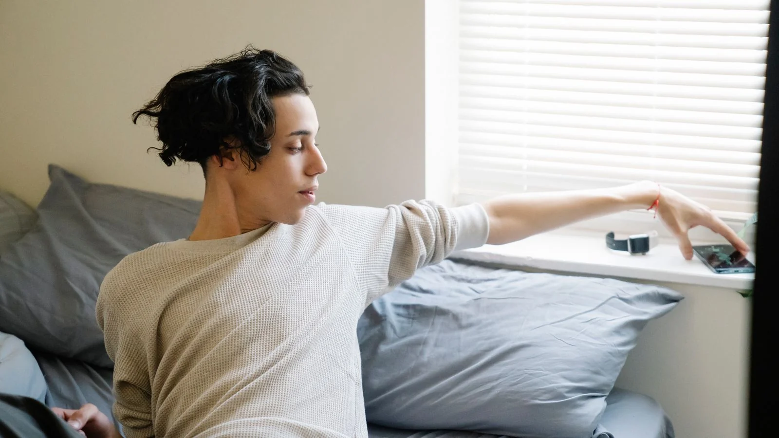 Teenager reaching for a phone on the windowsill just after waking, the moment most newsletter opens are recorded
